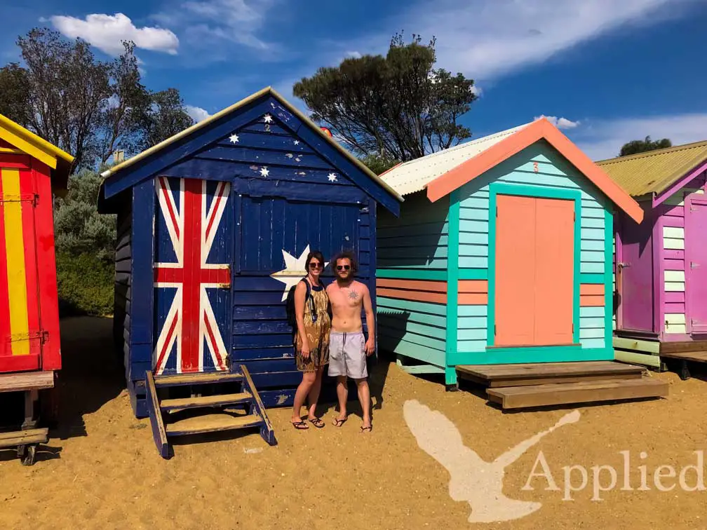 Photo of Luke and Stephanie standing in front of a brighton beach box painted with the Australian flag in Melbourne Australia