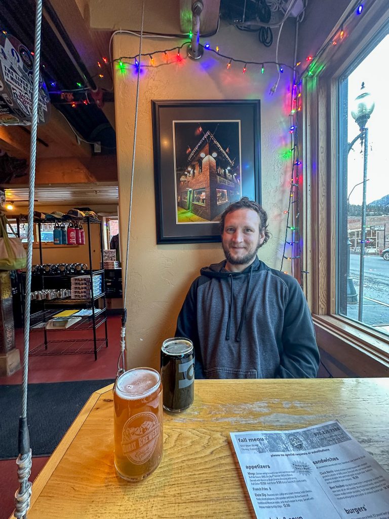 Luke siting at a small bar table at Ouray Brewery with two Colorado Craft Beers sitting in front of him.