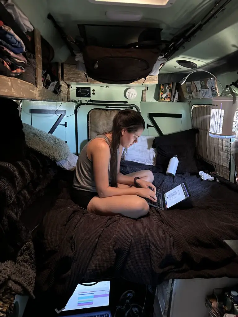 Photo of Stephanie working from bed in a cross-legged position hunched over her laptop for our blog on Transforming an Old Shack in the Desert into our Office.