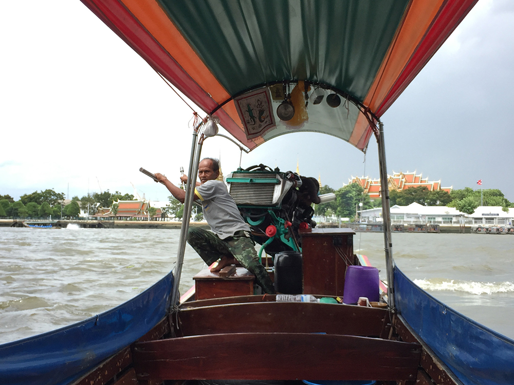 Photo of a boat on the river in Bangkok with a local man steering on the back for Applied Worldwide blog "4 Practical Tips to Plan a Vacation in Thailand Without the Stress"