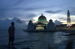 Photo of Luke Hanna staring out at the Mosque as it plays the call to prayer at sunset in Malacca, Malaysia.