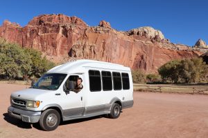 Photo of Luke Hanna waving out the driver's side window of his self-converted camper van in Capitol Reef National Park in Utah for a blog on Road Trips and Road Trip Culture in the United States