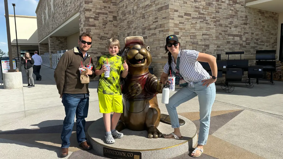 Photo of Luke, Stephanie, and their nephew Maverick posing outside of Buc-ee's in Johnstown, CO with the Buc-ee Beaver statue holding Icees for a blog titled "Visiting Buc-ee's and All it has to Offer"