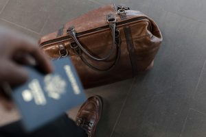 Photo of a brown leather bag taken in Birds Eye view with a passport blurbed in the foreground in a traveler's hand for Applied Worldwide Lifestyle blog titled "How to Travel Better: Stay Smart, Live Local, and Keep It Simple"
