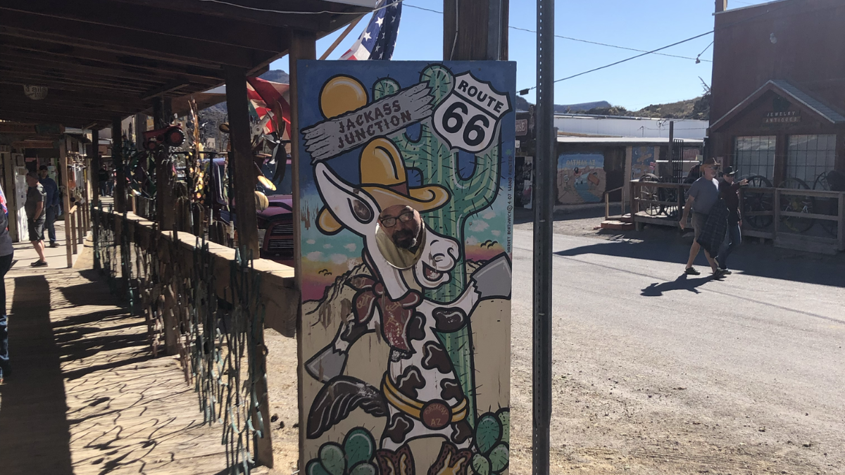 Photo of a Photo Booth sign in Oatman Colorado with a donkey that reads "Jackass Junction" and "Route 66" for Applied Worldwide blog "Ghost Towns in Arizona: Stories From the Desert’s Forgotten Places"