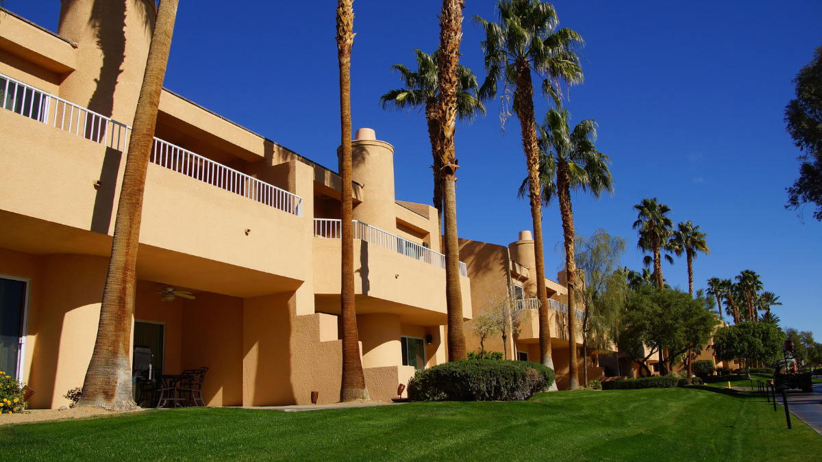 Photo of a sand colored timeshare condo with green grass and palm trees liking the property for Applied Worldwide blog "Timeshare Presentations: An Intrusive World"