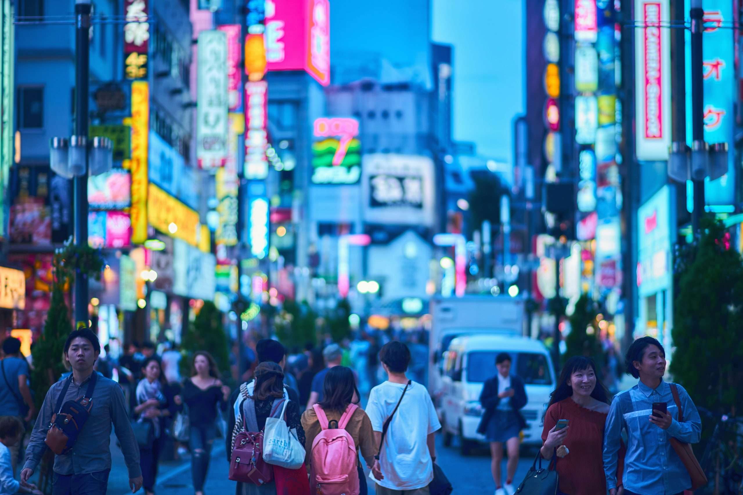 Poto of people in a busy city at dusk with high rise buildings and color lit-up signs all around for Applied Worldwide blog "New Ways to Experience a City in 2026"
