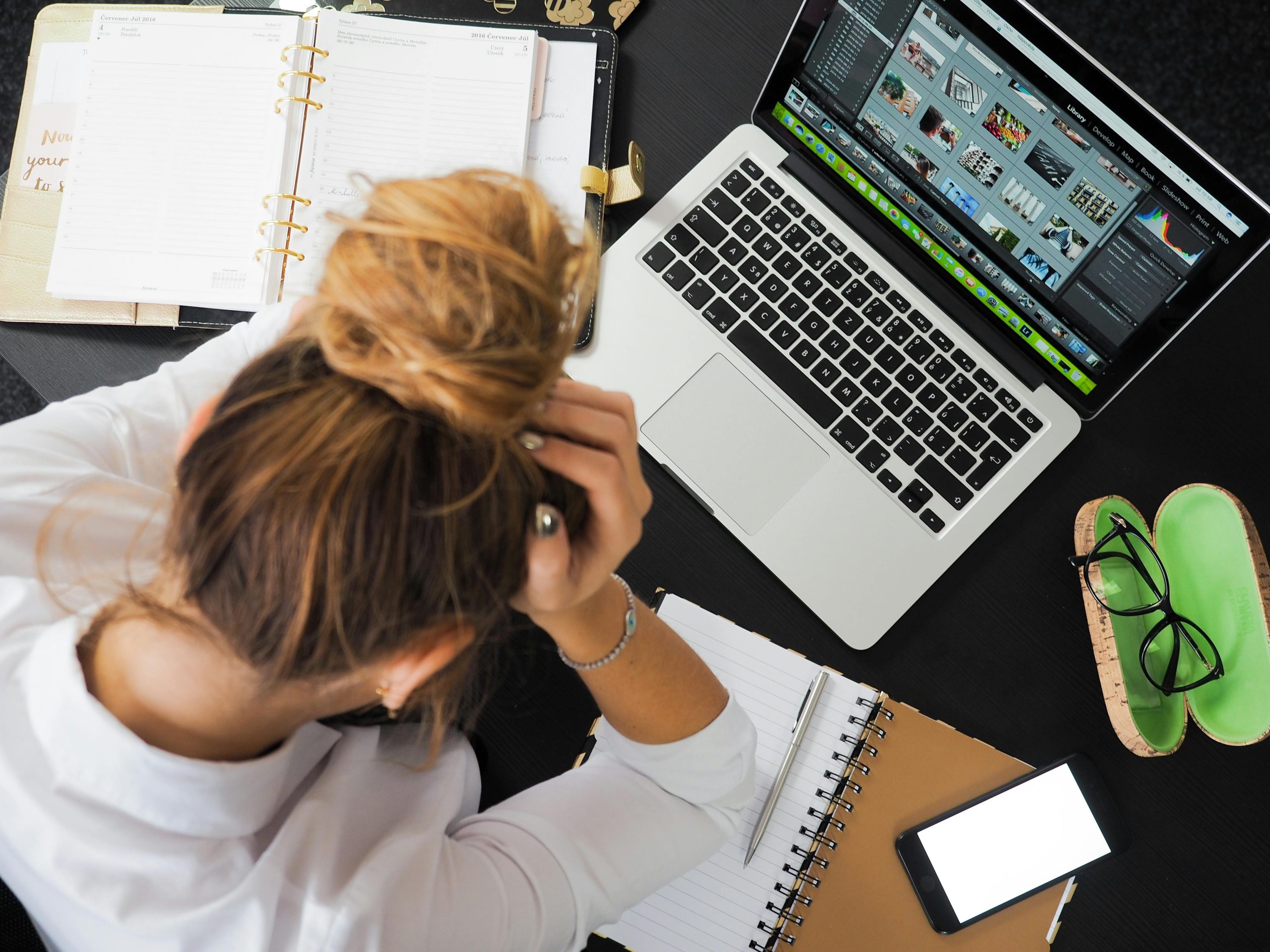 Birds Eye view of woman looking frustrated with a laptop in front of her and open notebooks for Applied Worldwide Lifestyle blog "Want to Work Abroad? Here are some Useful Tips"