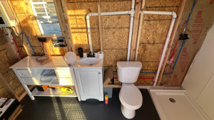 Photo of the unfinished wall of plumbing, showing a countertop, sink, toilet and shower base for Applied Worldwide Lifestyle blog "Why We Chose SharkBite Fittings for our Off-Grid Bathroom"