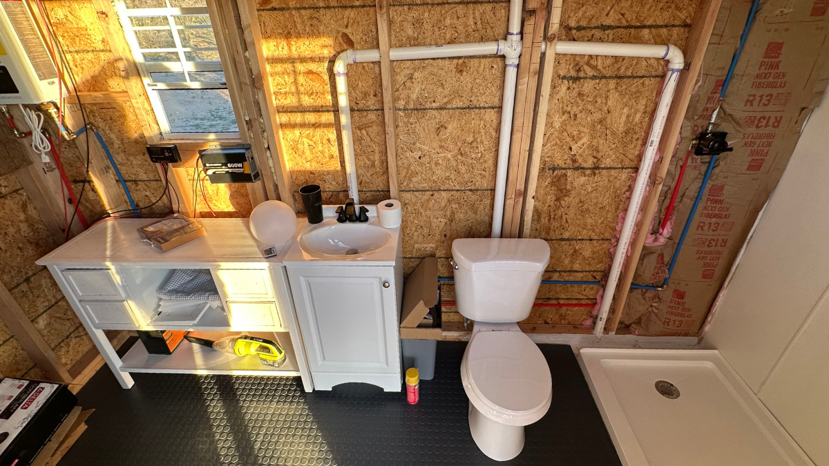 Photo of the unfinished wall of plumbing, showing a countertop, sink, toilet and shower base for Applied Worldwide Lifestyle blog "Why We Chose SharkBite Fittings for our Off-Grid Bathroom"