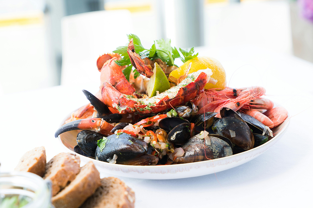 A bowl of muscles, crab legs, and shrimp with lemon and herbs for garnish for Applied Worldwide Lifestyle blog "5 Reasons to Serve Seafood at a Dinner Party"