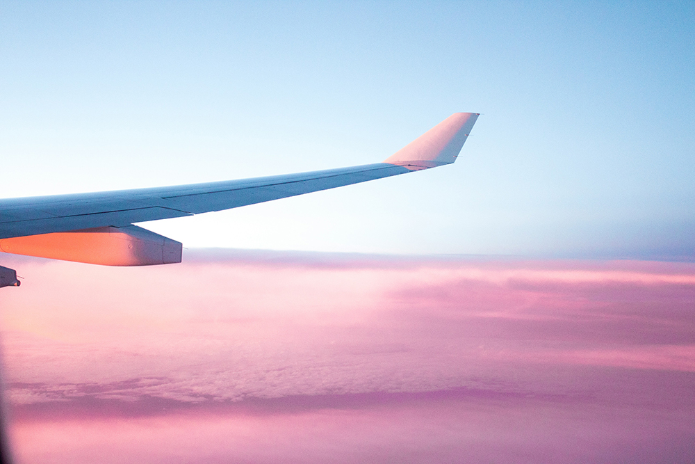 Photo of an airplane wing against a sky with pink clouds for Applied Worldwide Lifestyle blog "3 Essential Vacation Planning Tips to Have an Amazing Trip"