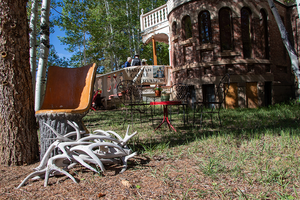 Hartman Castle tower under the shade of aspen trees with antlers and outdoor seating displayed on the lawn for Applied Worldwide blog "Hartman Castle Welcome Community for First Time in Century"