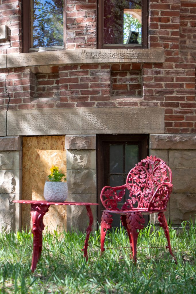 Ornate red cast iron table and chair with potted flowers sitting in from of the Hartman Castle tower for Applied Worldwide blog "Hartman Castle Welcome Community for First Time in Century"