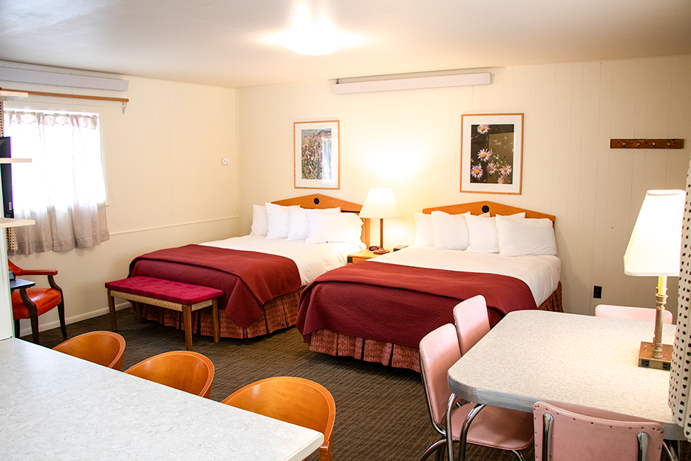 Photo of a Deluxe Queen Studio room at Island Acres Resort Motel showing two queen beds, a vintage chrome dining set, and the bar dividing the kitchen from the living space.