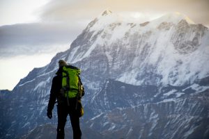 man in green jacket and black pants with black backpack standing on snow covered mountain during for Applied Worldwide blog "Travel Smart: Essential Gear for Cold Weather Journeys"